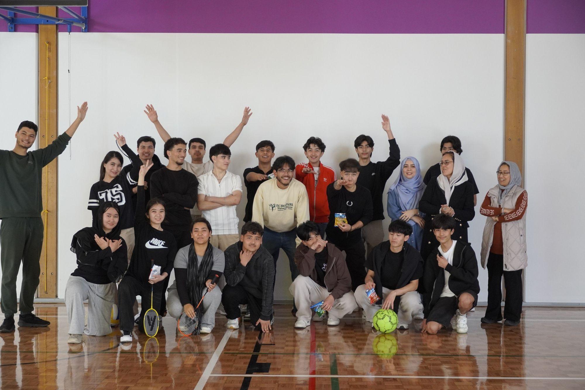 The whole group lined up against the hall wall after a badminton session, arms in the air