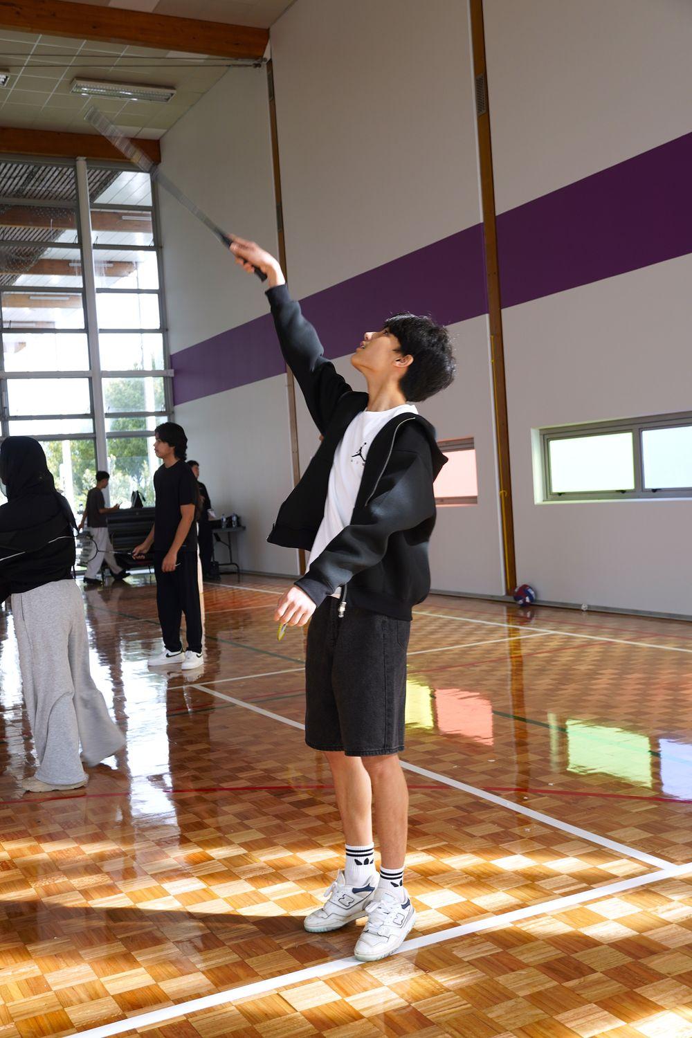 A player reaching up to return the shuttle, racket high, in afternoon light